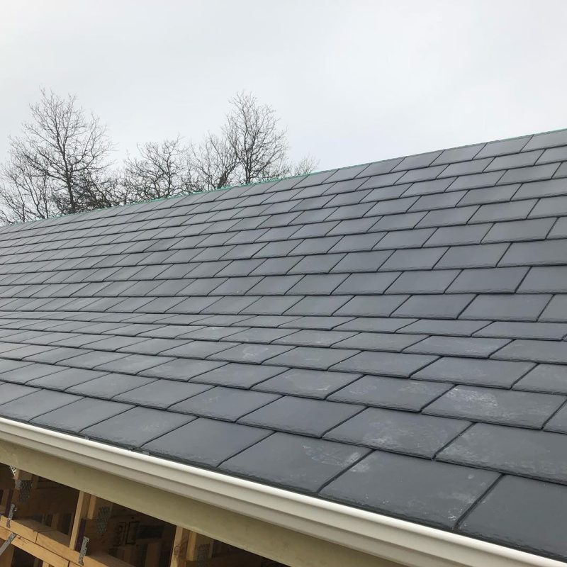 Close-up of a residential roof featuring high-quality, dark grey slate tiles installed with precise alignment.