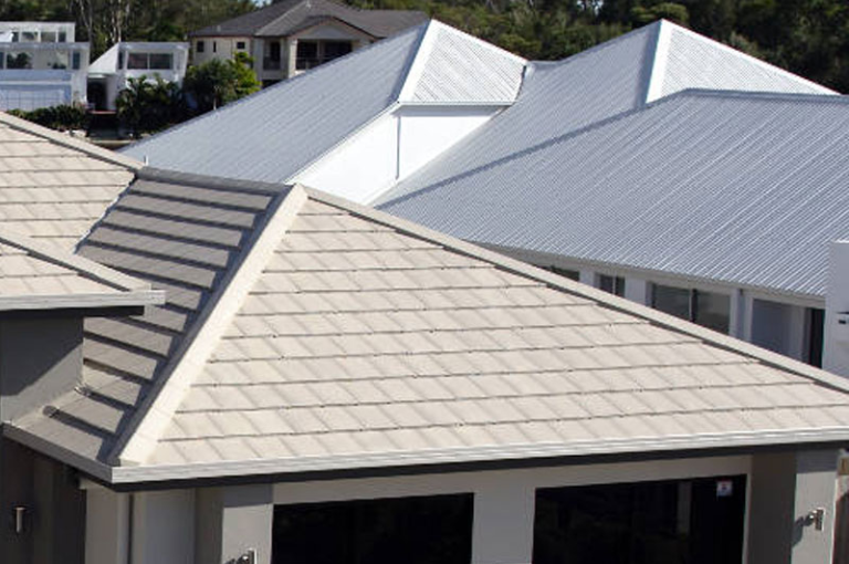 Elevated view of modern suburban homes featuring light-colored tiled roofing in the foreground and corrugated metal roofs in the background.